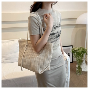 Detail view of a cream woven straw tote bag with slim shoulder straps for summer
