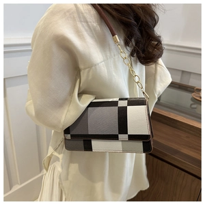 Close-up of a plaid crossbody bag with metal chain strap worn by a model