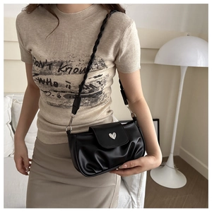 Detail of black pleated bag featuring silver heart buckle and braided shoulder strap
