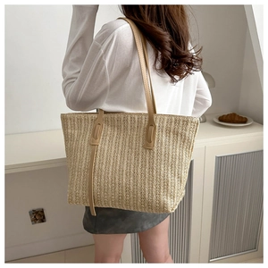 Detail of woven straw tote bag featuring brown leather shoulder straps and natural texture