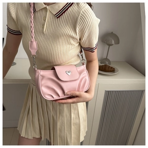 Pink pleated crossbody bag with heart buckle and braided strap on a model