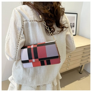 Detail of color-block flap bag with gold chain strap worn by a model in a soft room