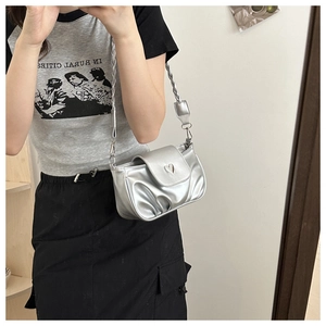 Close-up of silver pleated handbag featuring a heart metal buckle and braided strap