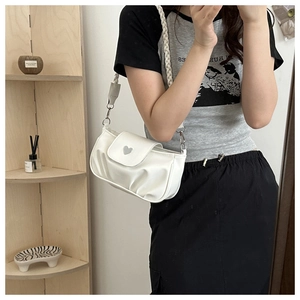 Detail of white pleated shoulder bag featuring a silver heart buckle and braided strap