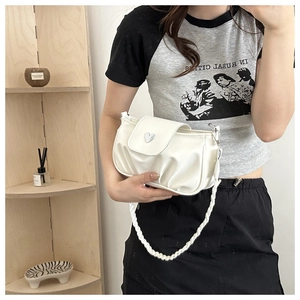 Detail of white pleated handbag featuring a silver heart-shaped clasp and braided strap
