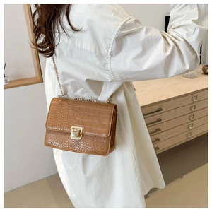 Détail du sac bandoulière marron gaufré crocodile avec chaîne dorée porté par un modèle
