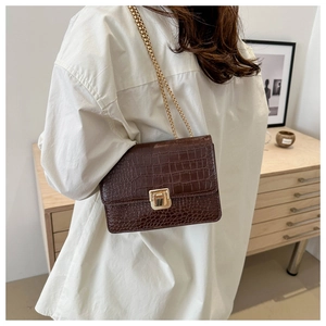 Détail d'un sac bandoulière marron foncé effet crocodile avec bandoulière chaîne dorée