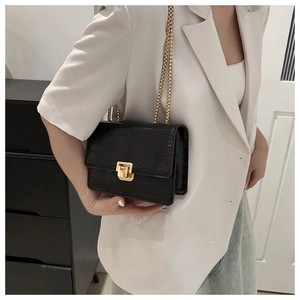Détail de sac noir à motif crocodile avec bandoulière chaîne dorée et fermoir