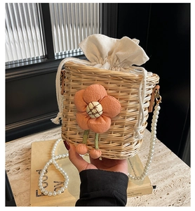 Detail of woven straw bucket bag featuring orange 3D flowers and white pearl strap