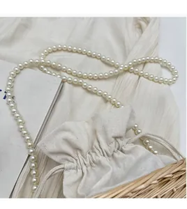 Detail of hand-woven straw bucket bag with pearl strap and white canvas drawstring liner