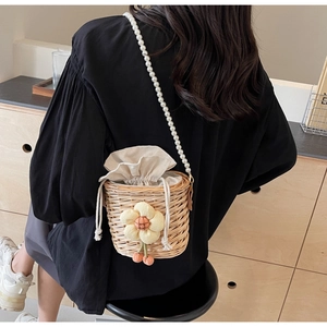 Detail of straw bucket bag with floral accent and elegant pearl beaded shoulder strap