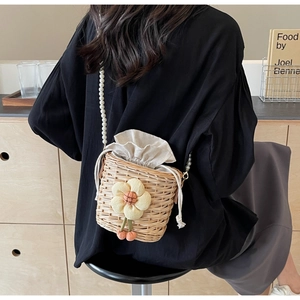 Detail of straw bucket bag featuring a decorative fabric flower and pearl shoulder strap