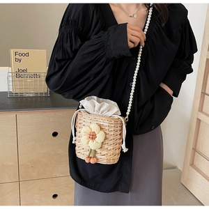 Detail of straw bucket bag featuring sunflower charm and elegant pearl shoulder strap