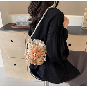 Detail of handmade straw bucket bag with pearl strap and decorative orange flower