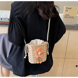 Detail of woven straw bucket bag with orange floral accent and pearl strap