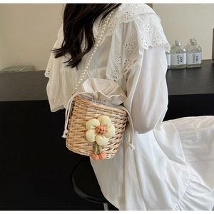 Detail of woven straw bucket bag featuring a pearl strap and 3D floral accent