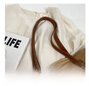 Detail of dark brown leather strap and hand-woven straw texture of the beach tote bag