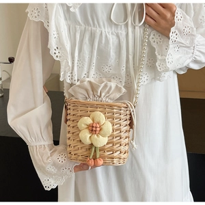 Detail of woven straw bucket bag featuring a yellow plush flower and pearl chain strap