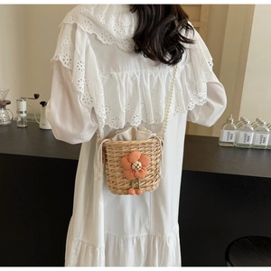 Artistic hand-woven straw bucket bag with floral accent and pearl strap on a model