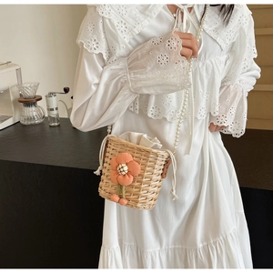 Detail of woven straw bucket bag with orange floral decor and pearl beaded strap