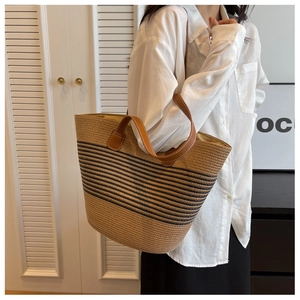 Close-up of woven straw tote with black stripes and brown leather handles with stitching