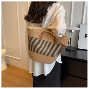 Detail of woven straw tote bag with black stripes and brown leather shoulder straps