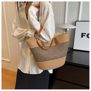 Detail of hand-woven straw tote bag with navy blue stripes and brown leather handle