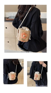 Detail of woven bucket bag featuring orange plush flower and pearl bead shoulder strap
