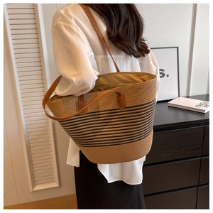 Model wearing a large striped straw tote bag with brown leather straps for beach holidays