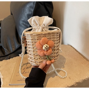 Detail of woven straw bucket bag with orange fabric flower and pearl chain strap