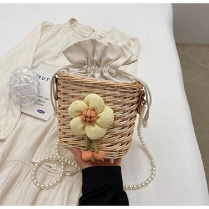 Detail of handwoven straw bucket bag with floral accent and faux pearl handle