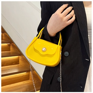 Detail of mini yellow PVC bag with pearl buckle and gold chain strap on a model