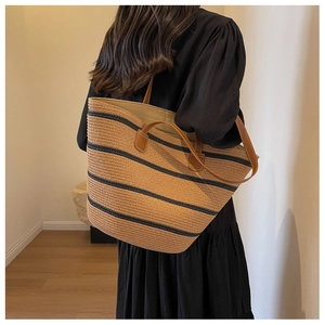 Close-up of a striped woven tote bag with brown leather handles and textured straw material