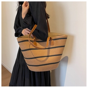 Close-up of woven straw tote bag featuring black stripes and brown leather handles