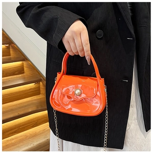 Macro shot of orange glossy PVC mini bag with pearl buckle and gold chain strap