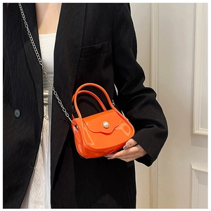 Mini orange PVC bag with glossy finish and pearl detail shown on a model