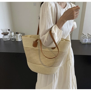 Close-up of woven straw tote bag with brown leather handles on a white dress