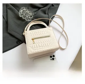 Mini cream crocodile pattern crossbody bag showing size comparison with a smartphone