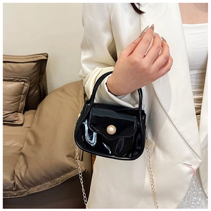 Close-up of black glossy mini bag featuring large pearl accent and gold chain strap