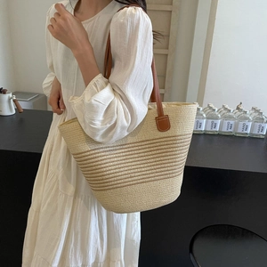 Detail of the woven straw tote bag featuring brown leather shoulder straps and reinforced seams