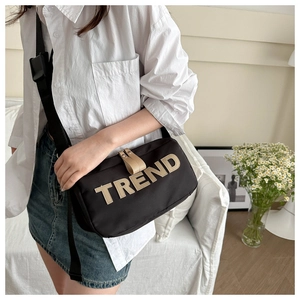 Detail of black nylon crossbody bag with TREND patch embroidery and wide strap in lifestyle setting
