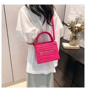 Detail of rose red croc-effect handbag worn by model against a minimalist home background