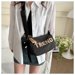 Detail of a black crossbody bag with TREND letter print and a cute plush ball charm