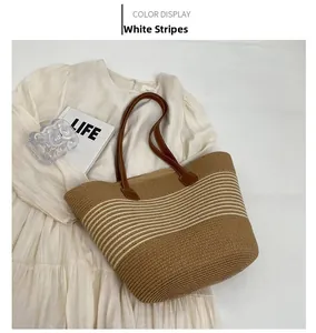 Detailed top view of a woven straw tote bag with white stripes and brown leather handles