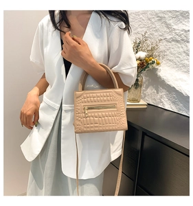 Detail of elegant beige crocodile pattern crossbody bag with round handle and leather strap