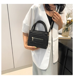 Detail of elegant black crocodile pattern handbag with metal zipper and leather strap