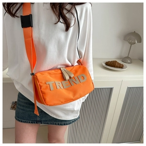 Detail of orange nylon crossbody bag with TREND letter patch and wide strap worn by model