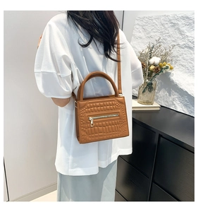 Brown crocodile pattern crossbody bag showing texture detail worn by a model in a room
