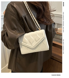 Detailed view of white wave quilted shoulder bag with elegant gold chain strap worn by model