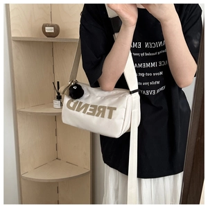 Close-up of white canvas crossbody bag with TREND letter detail and black pompom charm